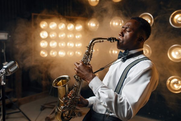 Black jazz performer plays the saxophone on the stage with spotlights. Black jazzman preforming on the scene